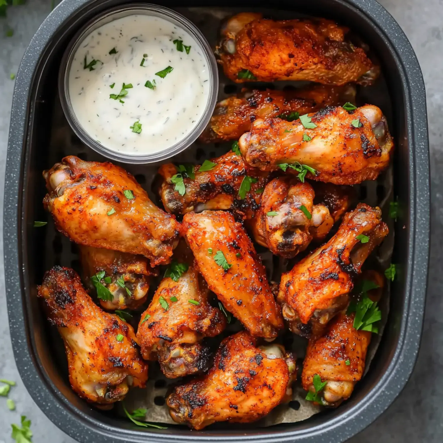 A tray of crispy, seasoned chicken wings garnished with parsley, accompanied by a small bowl of dipping sauce.