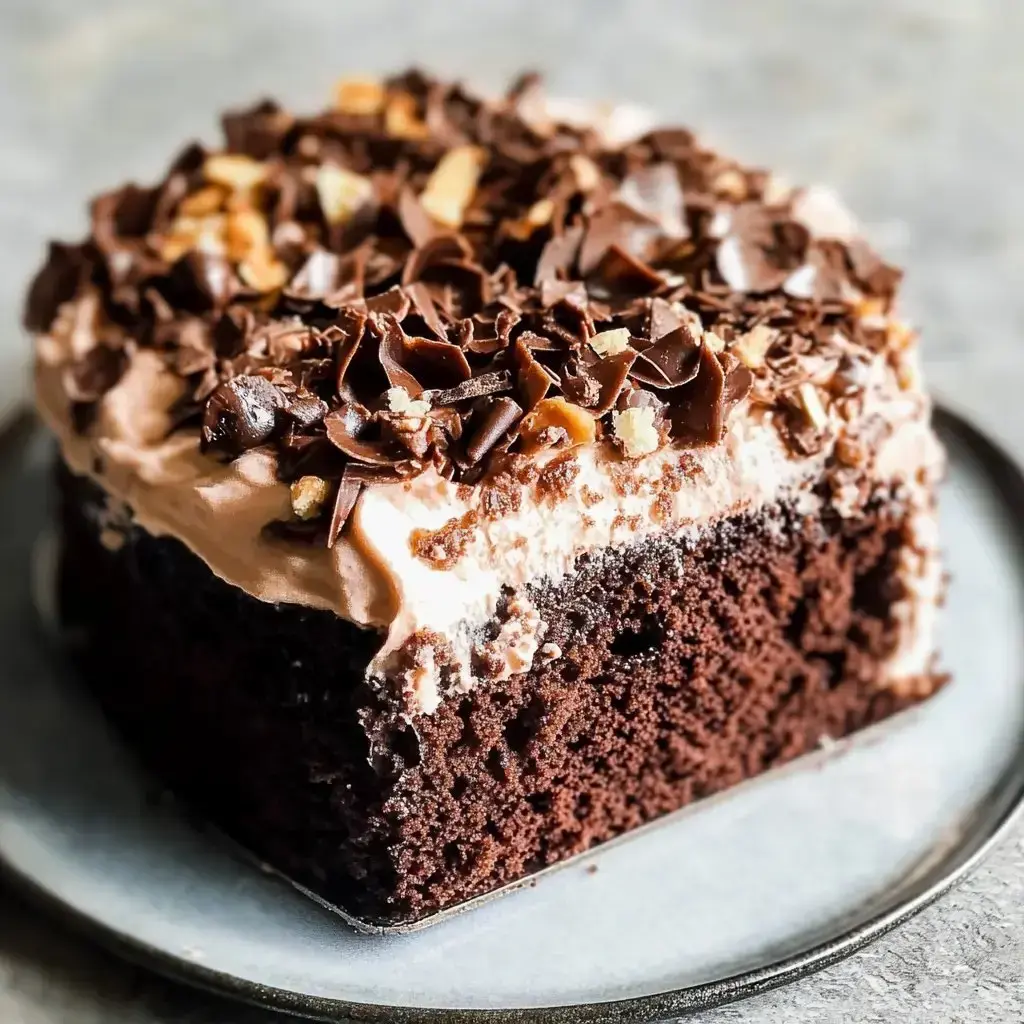 A decadent chocolate cake topped with chocolate shavings and cream, displayed on a gray plate.