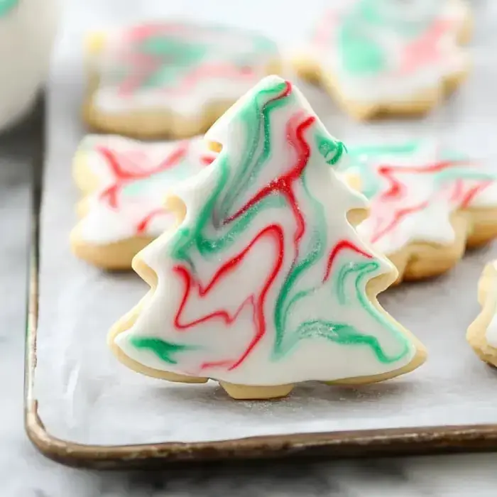 A decorated sugar cookie shaped like a Christmas tree, featuring red and green marbled icing.