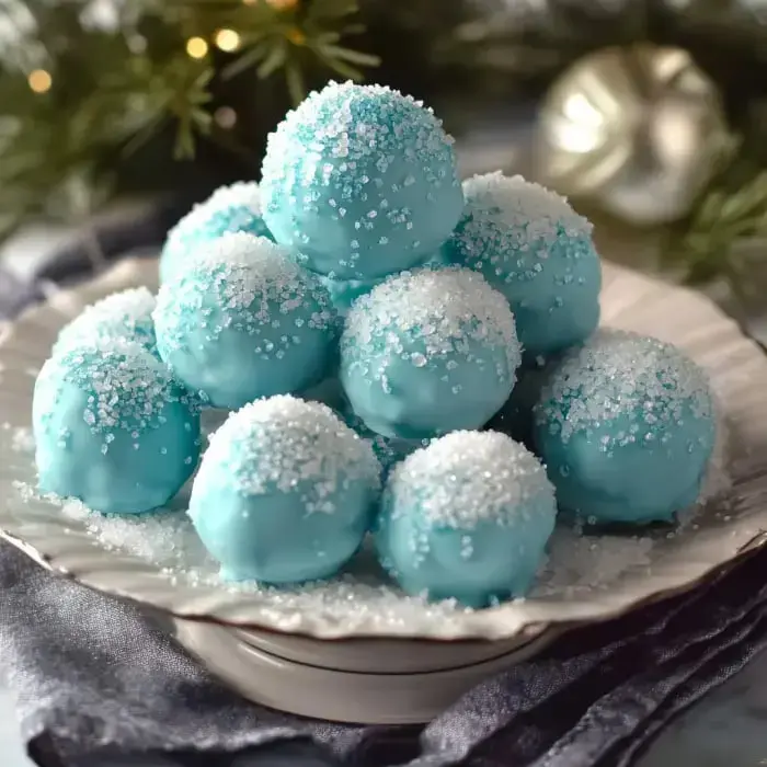 A plate stacked with light blue dessert balls coated in sugar, resembling a snowy arrangement, surrounded by festive greenery.