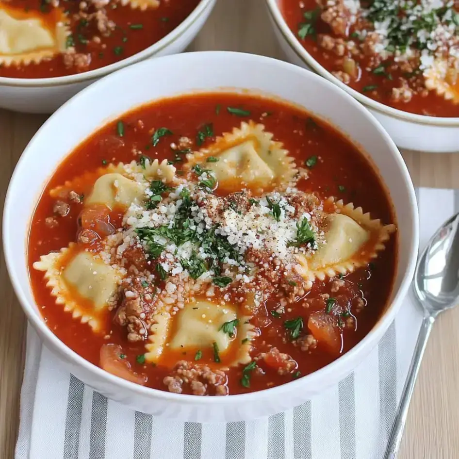 A bowl of ravioli soup featuring meat, tomato sauce, and garnished with parsley and grated cheese.