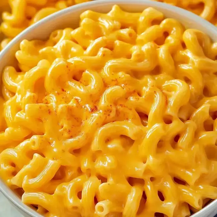 A close-up of a bowl filled with creamy macaroni and cheese topped with a sprinkle of paprika.