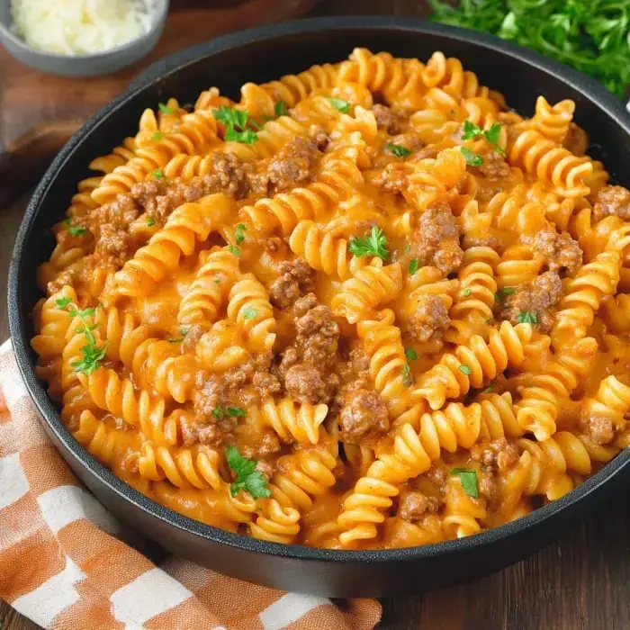 A close-up of a bowl of spiral pasta mixed with a creamy tomato sauce and ground meat, garnished with fresh parsley.