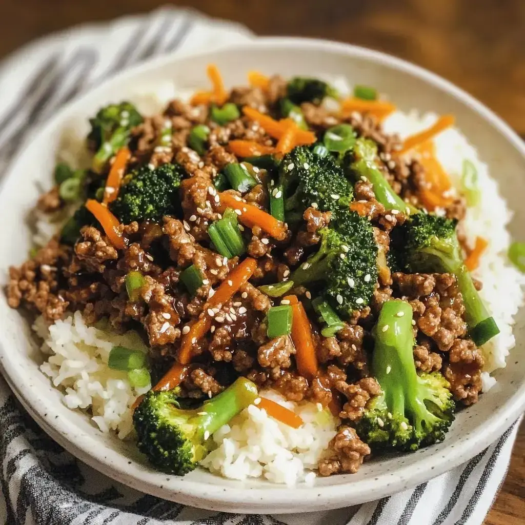 A bowl of rice topped with stir-fried ground meat, broccoli, carrots, and green onions, garnished with sesame seeds.