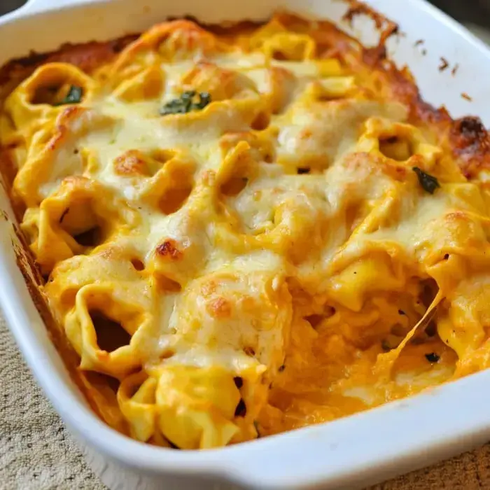 A baked pasta dish with cheese, featuring tortellini in a creamy sauce and garnished with green herbs.