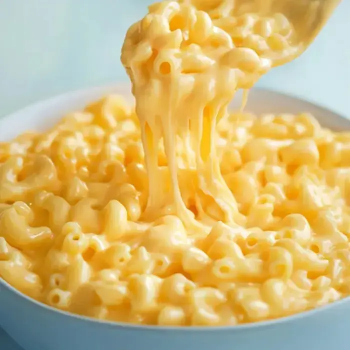 A spoon lifts creamy macaroni and cheese from a bowl, showcasing its rich, gooey texture.