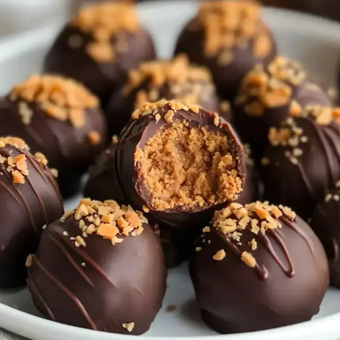 A close-up of chocolate-coated dessert balls, some topped with crushed nuts, with one ball showing a bite taken out to reveal a creamy filling.