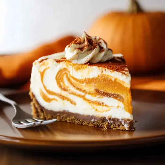 A slice of pumpkin cheesecake with a creamy swirl, topped with whipped cream and surrounded by autumn-themed decor.