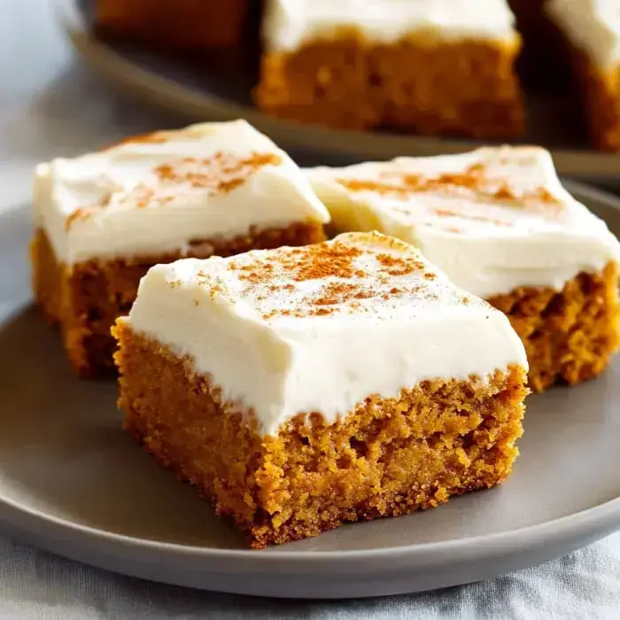 A plate of pumpkin bars topped with cream cheese frosting and sprinkled with cinnamon.