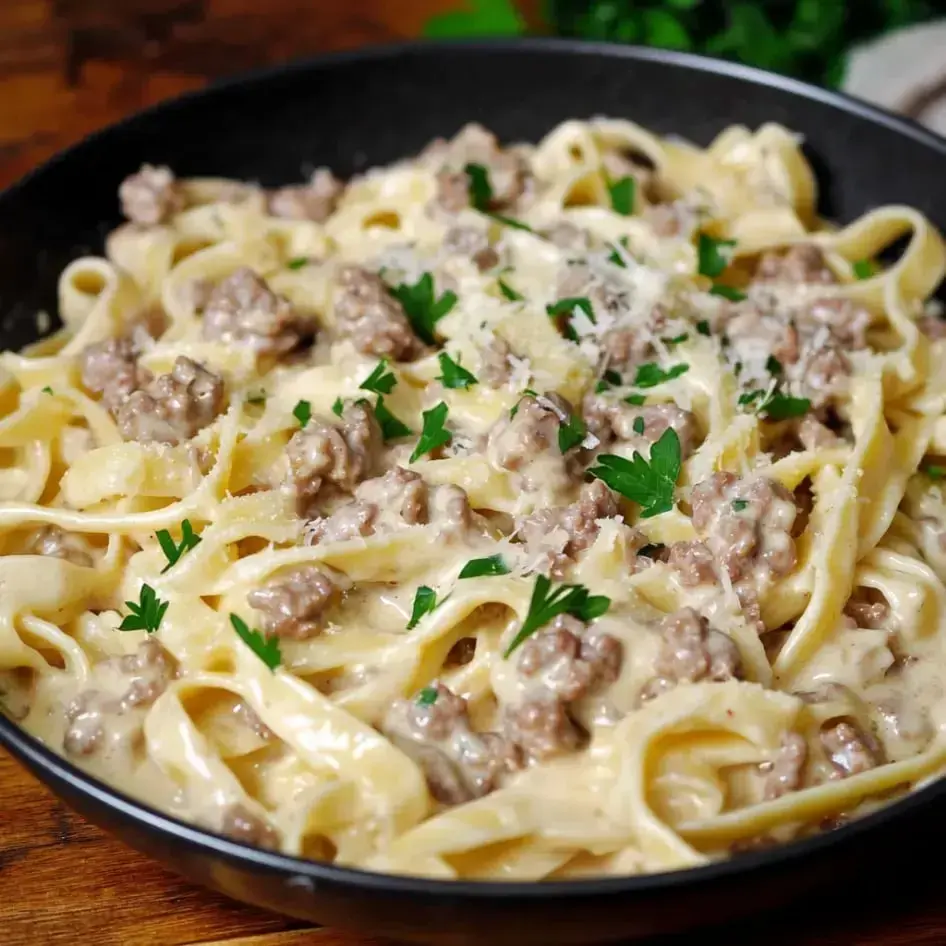 A bowl of creamy fettuccine pasta topped with ground meat and garnished with parsley.