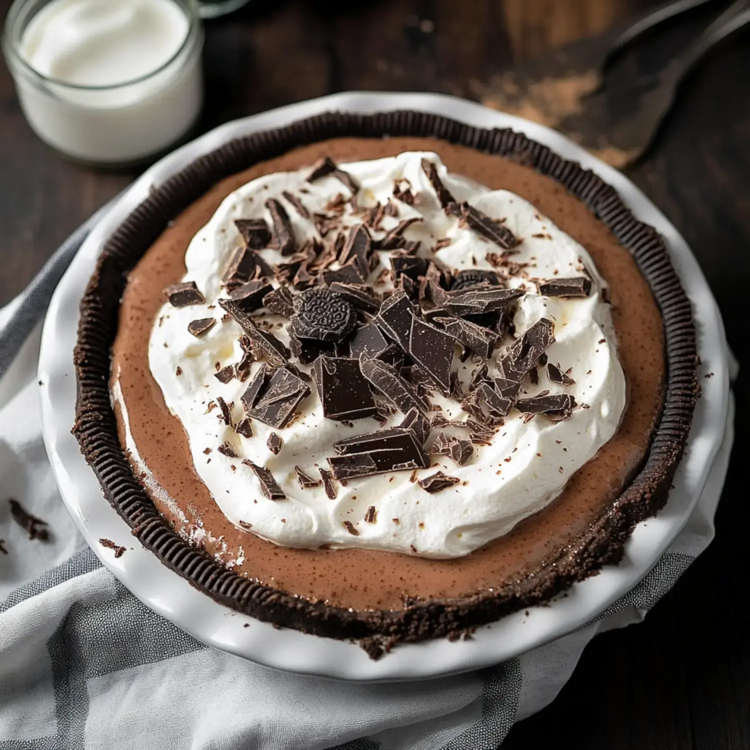 A chocolate cream pie topped with whipped cream and chocolate shavings, displayed on a white dish.