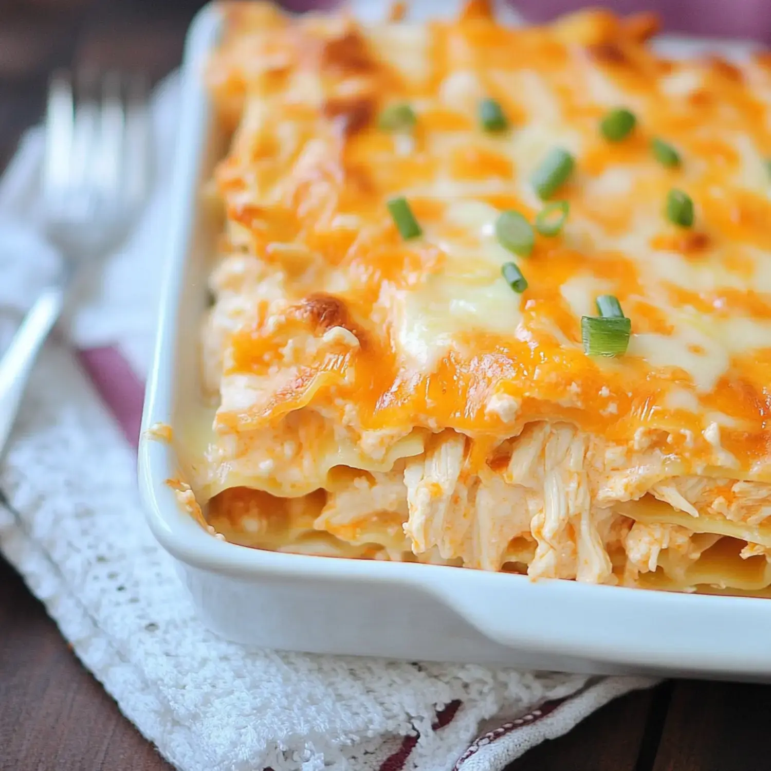 A casserole dish filled with cheesy, chicken lasagna topped with green onions.