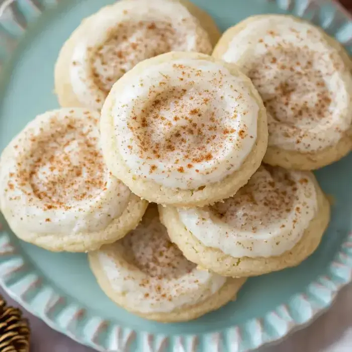 A stack of soft sugar cookies topped with creamy frosting and sprinkled with cinnamon on a light blue plate.