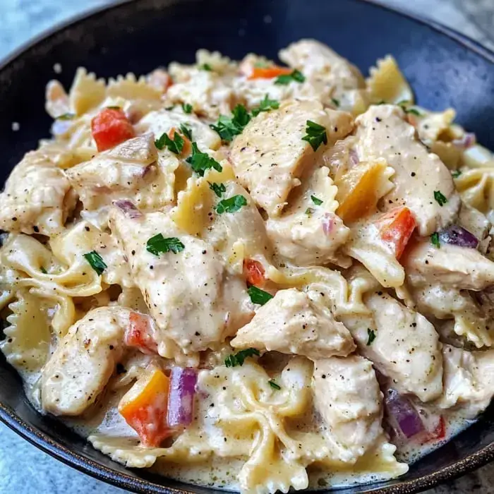 A bowl of creamy pasta with chicken, bell peppers, and garnished with parsley.