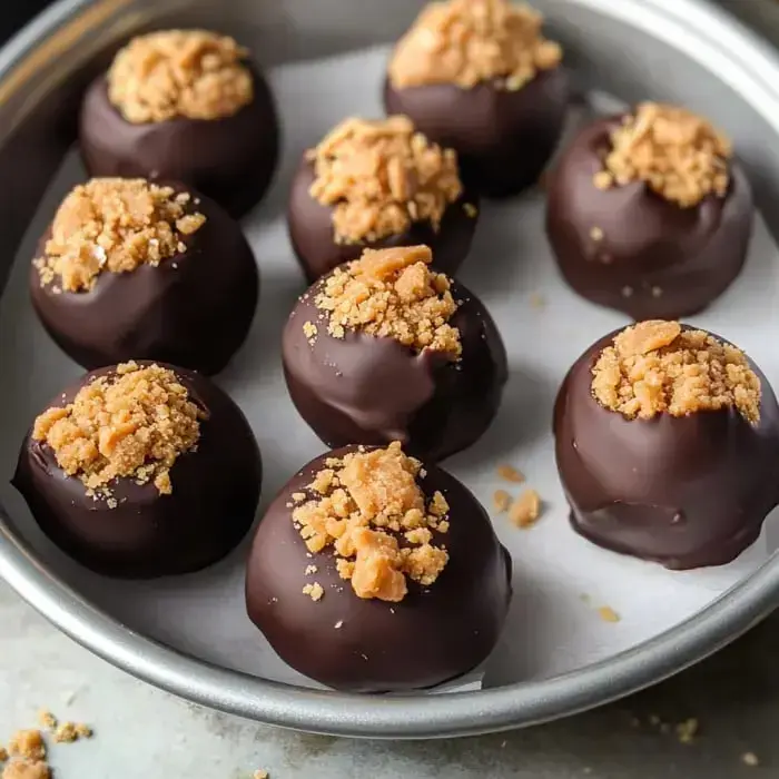 A silver platter holds several chocolate-covered truffles topped with crushed cookies.