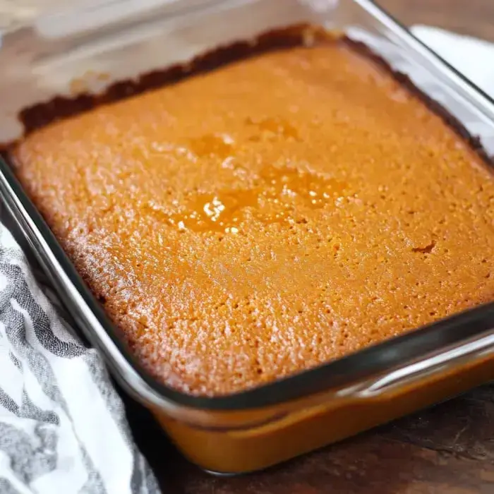 A freshly baked golden-brown cake in a glass baking dish, sitting on a wooden surface.