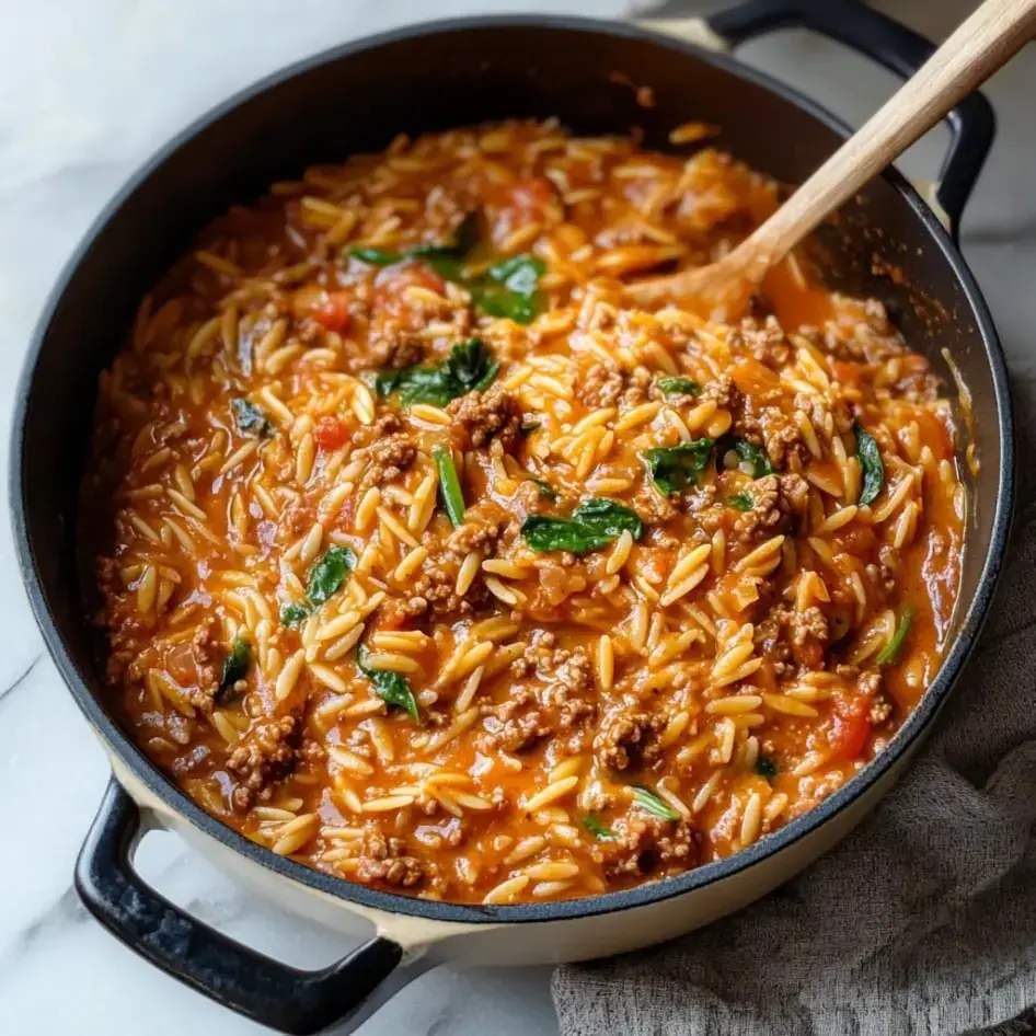 A pot of creamy orzo pasta mixed with ground meat, spinach, and diced tomatoes.