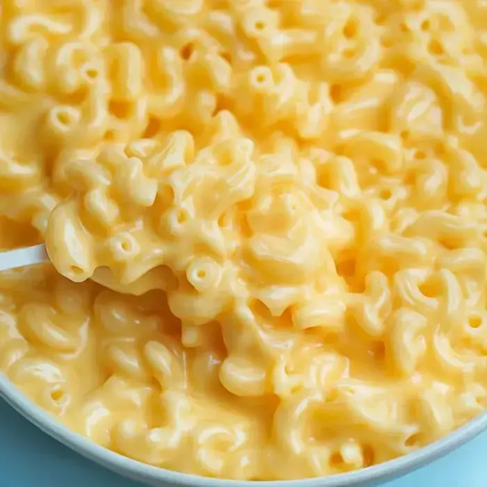 A close-up of a bowl of creamy macaroni and cheese with a spoonful lifted above.