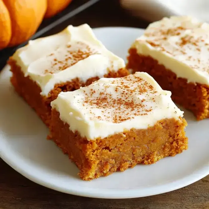 A plate of frosted pumpkin bars topped with a sprinkle of cinnamon.