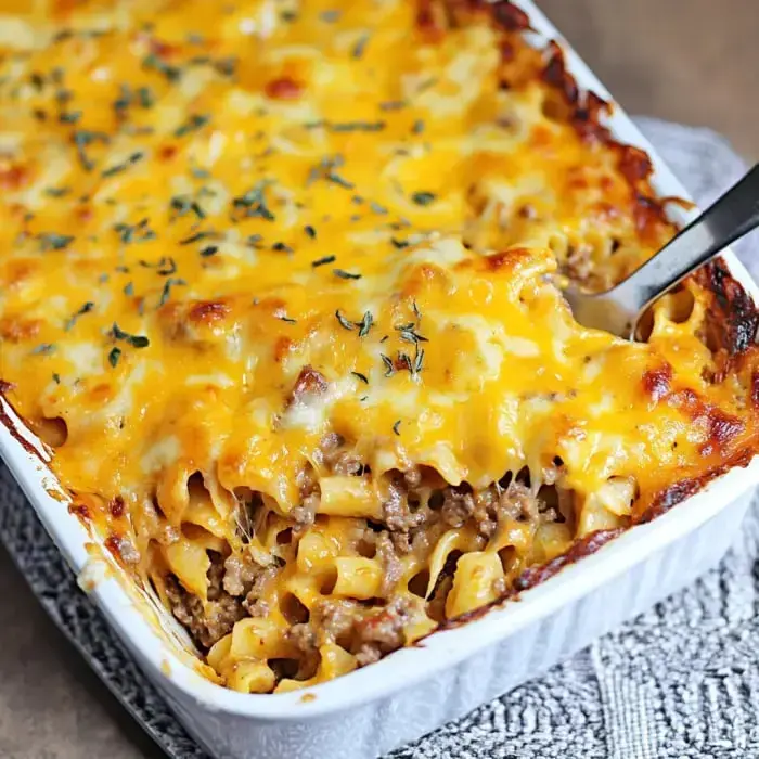 A cheesy casserole with pasta and ground beef, topped with melted cheddar and sprinkled with herbs.