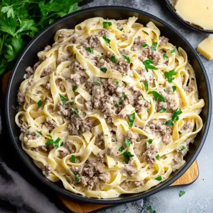 A bowl of creamy fettuccine pasta topped with seasoned ground meat and garnished with fresh parsley.