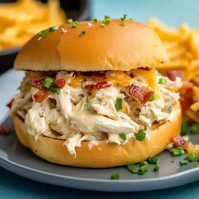 A shredded chicken sandwich topped with bacon, cheese, and green onions, served with a side of fries.