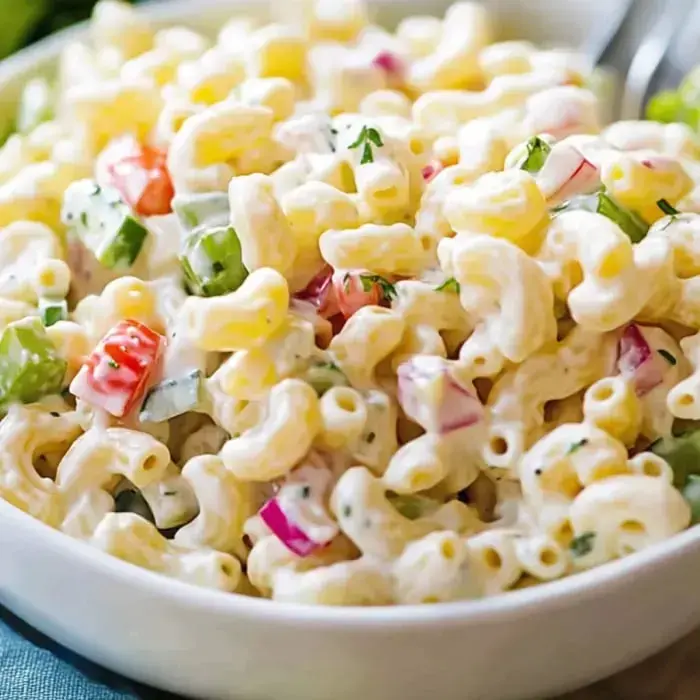 A close-up image of creamy macaroni salad mixed with diced vegetables including red peppers, green peppers, and onions in a white bowl.