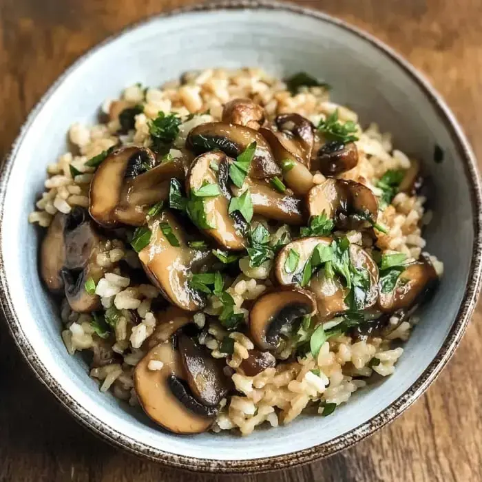 A bowl of brown rice topped with sautéed mushrooms and chopped parsley.