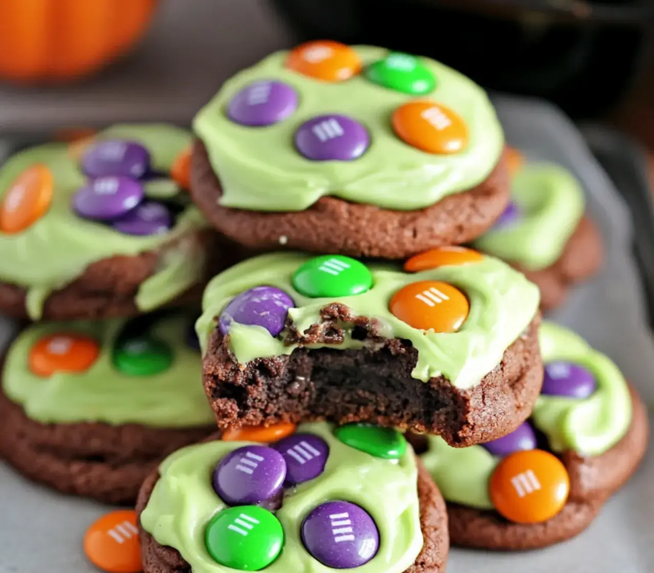 A stack of chocolate cookies topped with bright green icing and colorful candy pieces, with one cookie partially bitten.