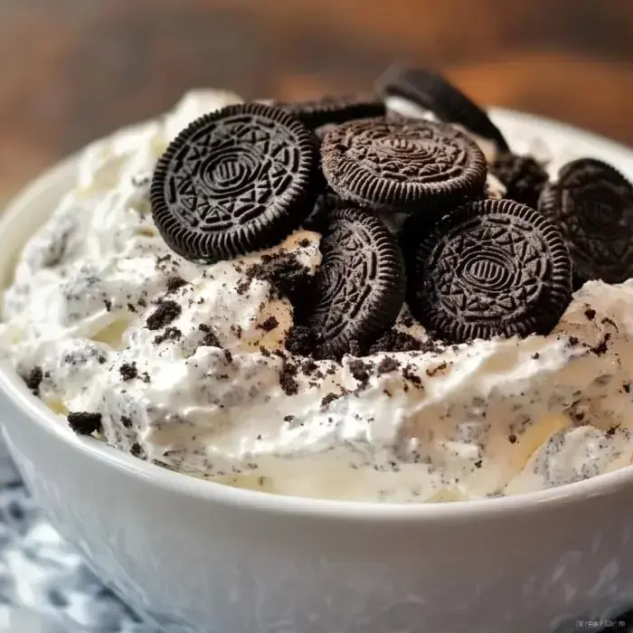 A bowl of whipped cream topped with crushed Oreo cookies and whole Oreos.