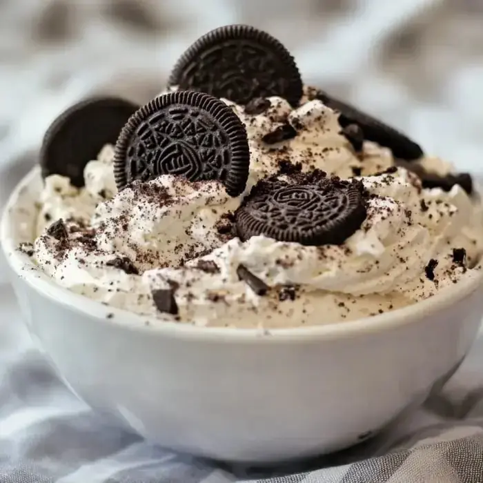 A bowl of whipped cream topped with crushed Oreos and whole Oreo cookies.