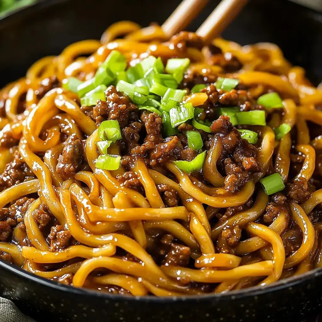 A close-up of a bowl of noodles topped with ground meat and chopped green onions.