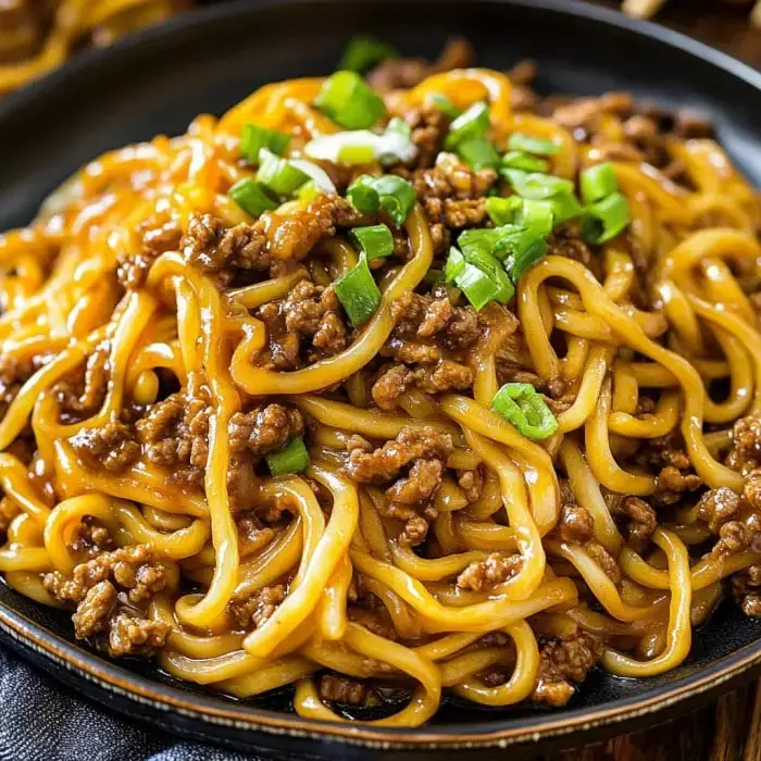 A close-up view of a plate of noodles topped with ground beef and chopped green onions.