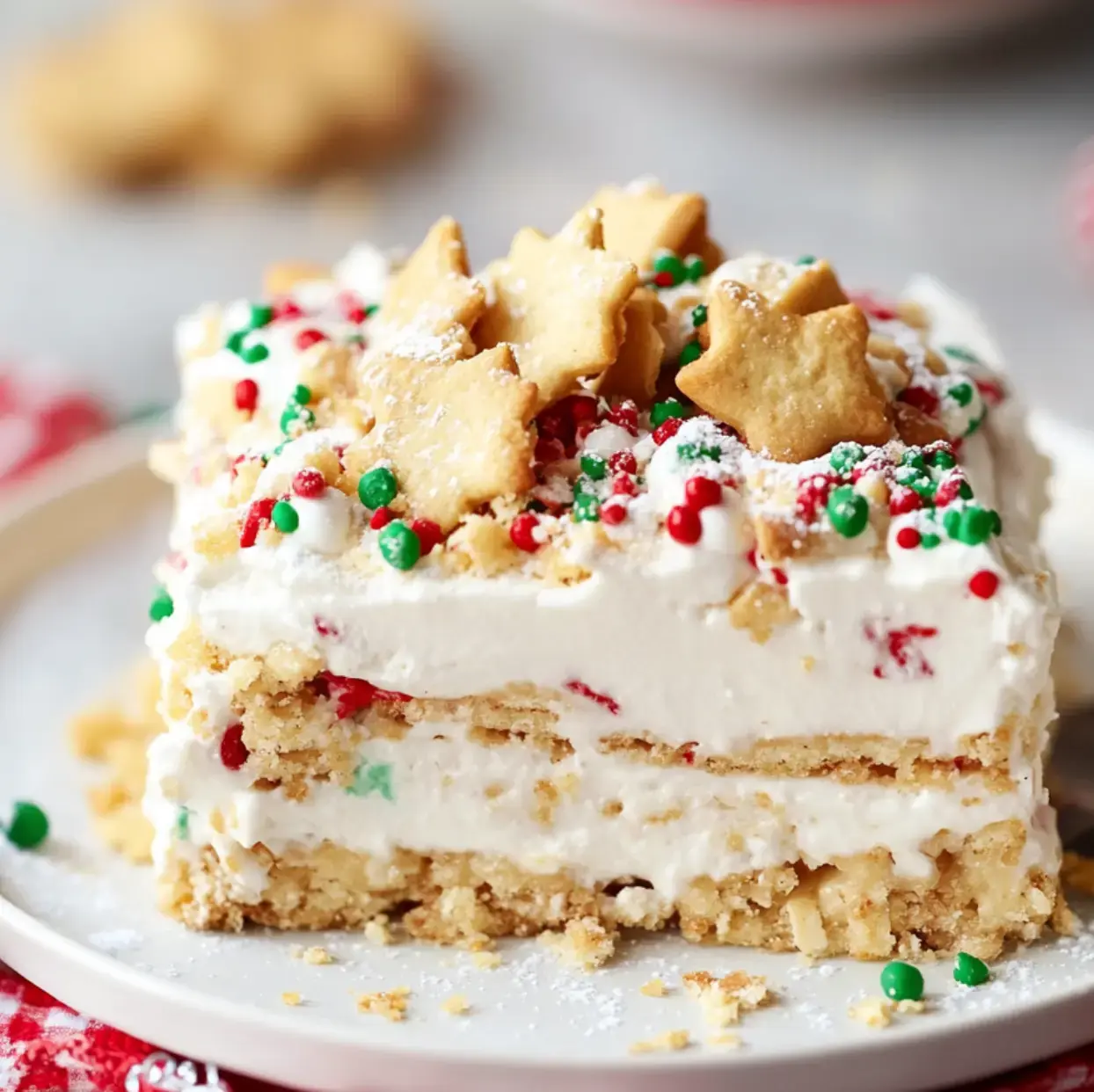 A slice of layered dessert topped with whipped cream, colorful sprinkles, and star-shaped cookies on a white plate.