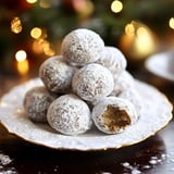 A plate of powdered sugar-coated dessert balls is stacked high, with one ball showing a bite taken out of it.