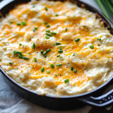 A creamy mashed potato dish topped with melted cheddar cheese and sprinkled with chopped green onions.