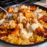 A close-up of a plate of yellow rice topped with pieces of grilled chicken, drizzled with creamy sauce and barbecue sauce.