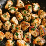 Sautéed pieces of chicken are garnished with chopped parsley in a skillet.