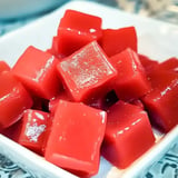 A close-up view of shiny red gelatin cubes stacked in a white dish.