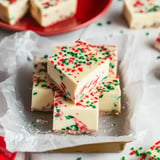 A stack of festive white fudge squares topped with red and green sprinkles on a gold tray.