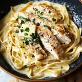 A delicious serving of fettuccine Alfredo topped with grilled chicken, butter, parsley, and grated cheese.