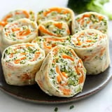 A plate of colorful rolled wraps filled with cream cheese, broccoli, and carrots.