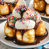 A plate of dessert featuring stacked, breaded and fried ice cream balls topped with colorful sprinkles and drizzled with chocolate sauce.