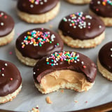 A close-up of chocolate-covered cookies with colorful sprinkles, displaying one cookie cut in half to reveal a creamy peanut butter filling.