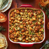 A dish of golden-brown stuffing with green peas, served in a red baking dish on a wooden table, accompanied by candles and decorative plates.