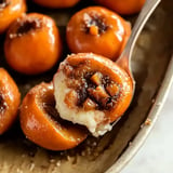 A close-up of roasted peaches filled with a cinnamon-sugar mixture and creamy filling, served on a plate.