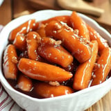 A bowl of glazed, cooked carrots coated in a sweet sauce.