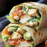 A close-up of two chicken wraps filled with lettuce, tomatoes, and creamy dressing, showcasing a toasted tortilla.