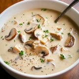 A bowl of creamy mushroom soup sprinkled with fresh herbs and black pepper.