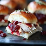 A close-up of a delicious slider sandwich filled with shredded chicken and cranberry sauce, garnished with a sprig of rosemary.